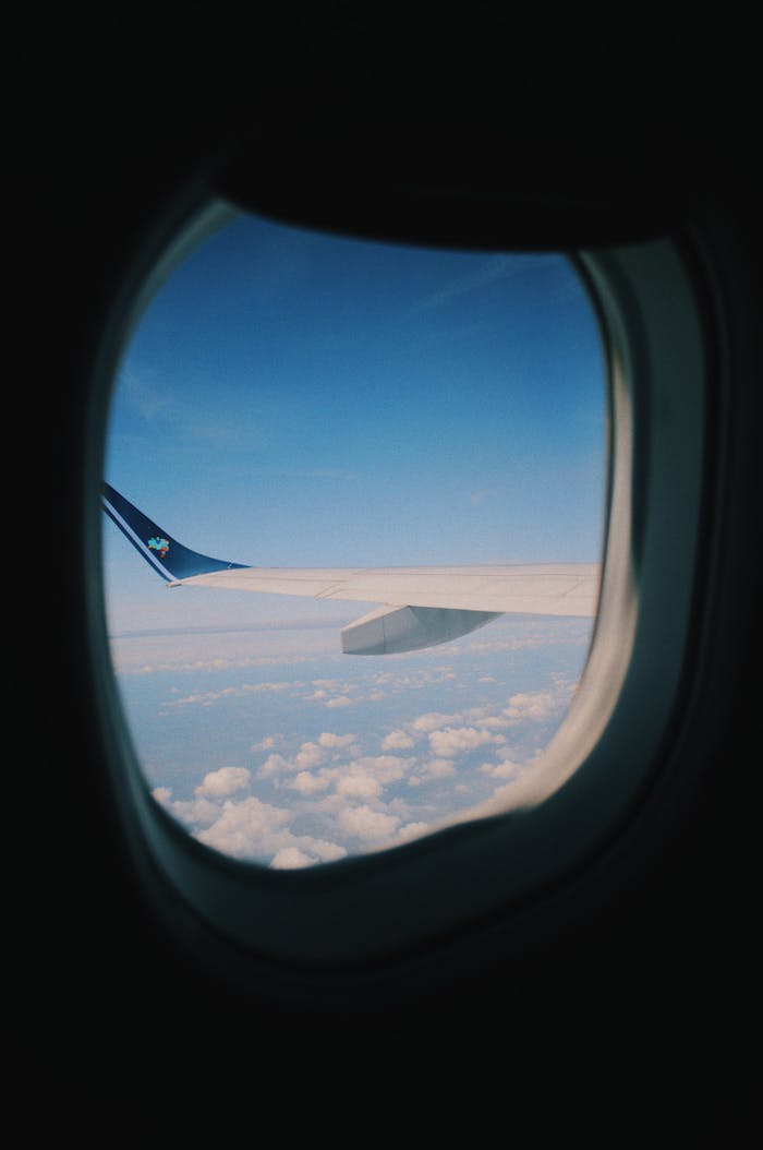 A serene view of sky and clouds through an airplane window, showcasing the aircraft wing.